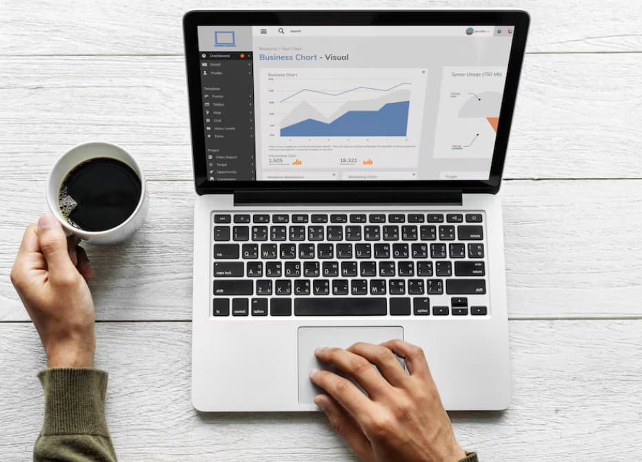 A person holding a cup of coffee while working on a laptop displaying business charts.